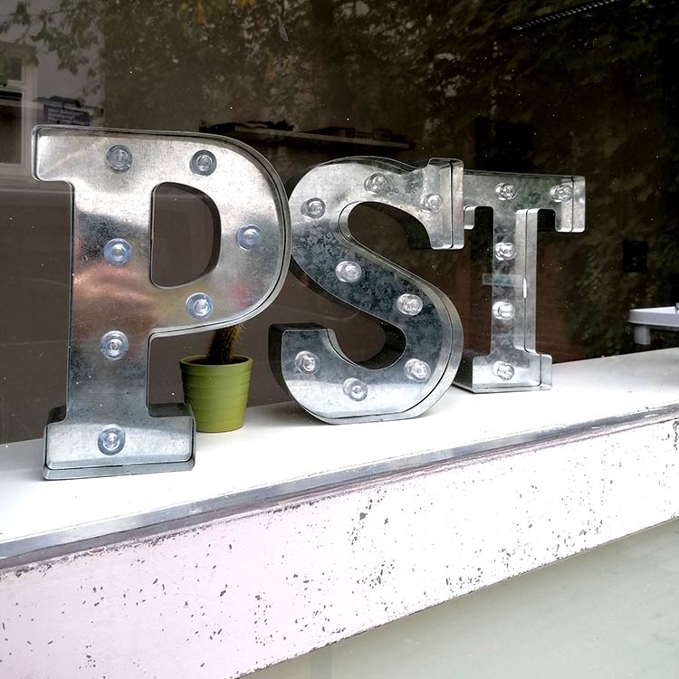 Metallene Leuchtbuchstaben P, S und T mit sichtbaren Glühbirnen auf einer Fensterbank